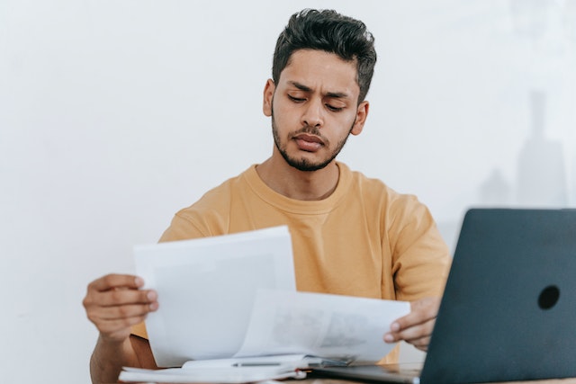 a property manager with short black hair and a close cropped beard reviews a tenant application at their desk while wearing a yellow crewneck sweater